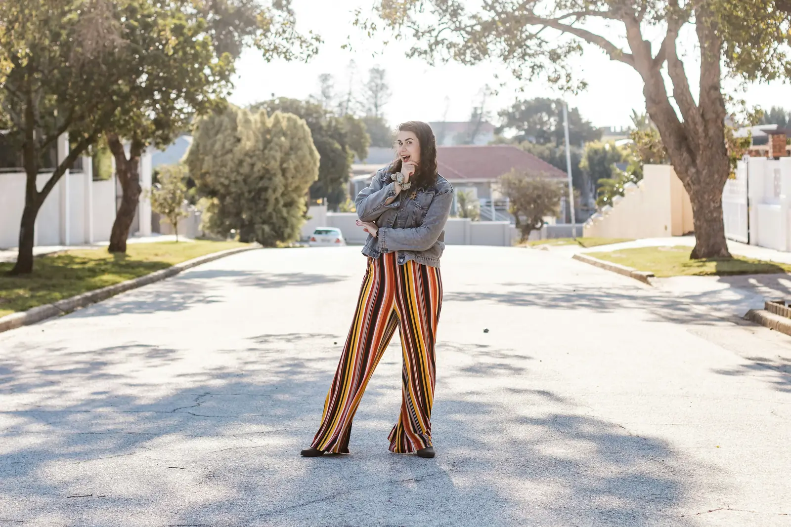 Woman in high-rise striped wide-leg trousers and a denim jacket standing on a sunlit street